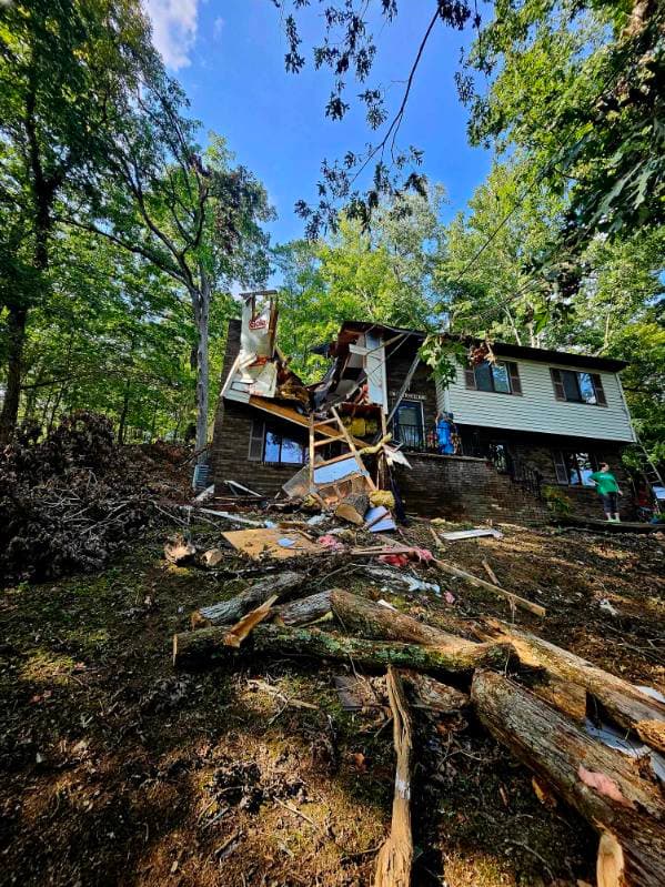 Storm damage to a home with fallen trees and damaged exterior walls